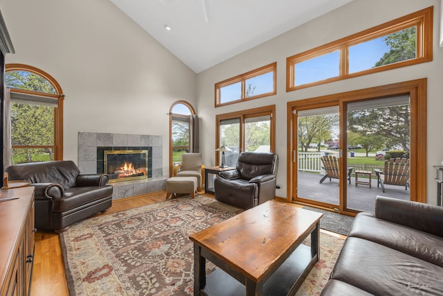living room featuring high vaulted ceiling, light wood-style flooring, and a tiled fireplace