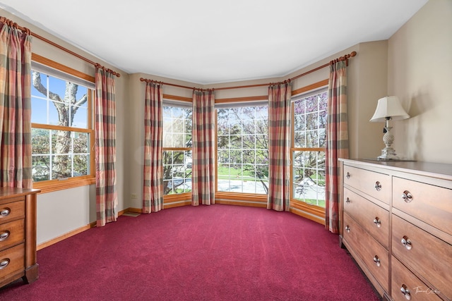 unfurnished room with plenty of natural light, dark colored carpet, and baseboards