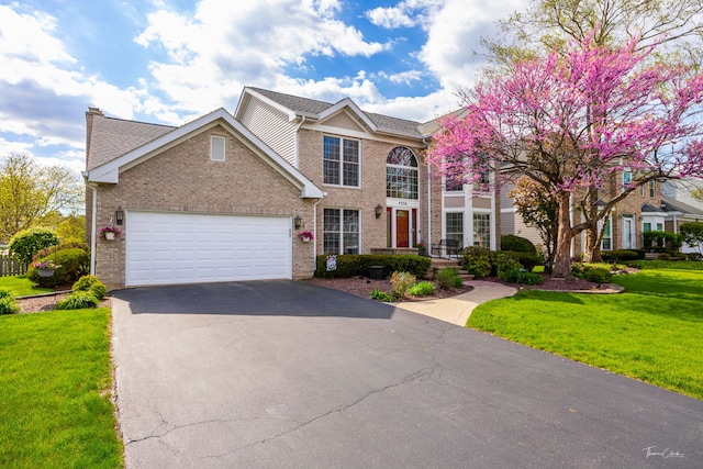 view of front of house featuring asphalt driveway, a front lawn, brick siding, an attached garage, and a chimney
