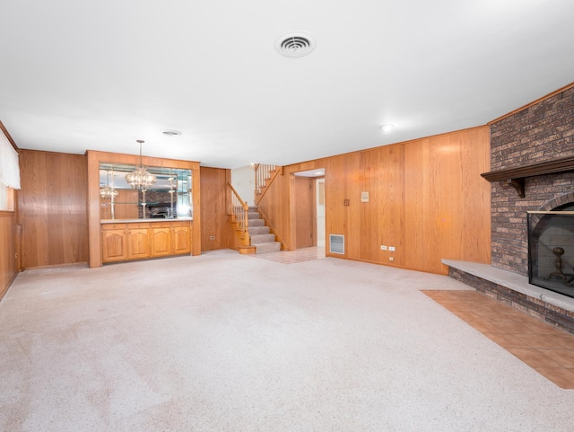 unfurnished living room with visible vents, a brick fireplace, wooden walls, and stairway