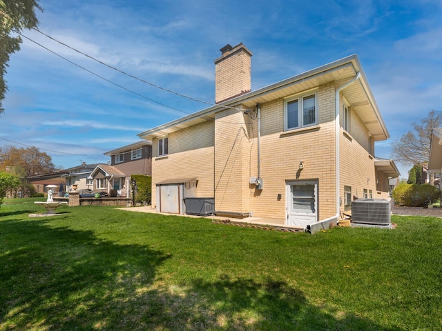 back of property featuring a lawn, a chimney, cooling unit, and brick siding