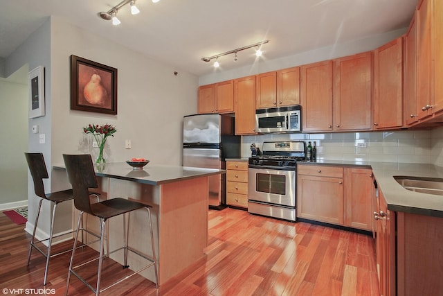 kitchen featuring stainless steel appliances, a peninsula, light wood-style floors, a breakfast bar area, and track lighting