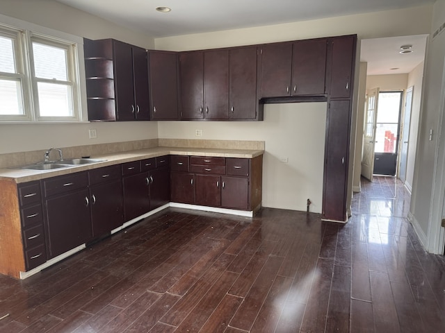 kitchen with a sink, open shelves, dark brown cabinetry, light countertops, and dark wood finished floors