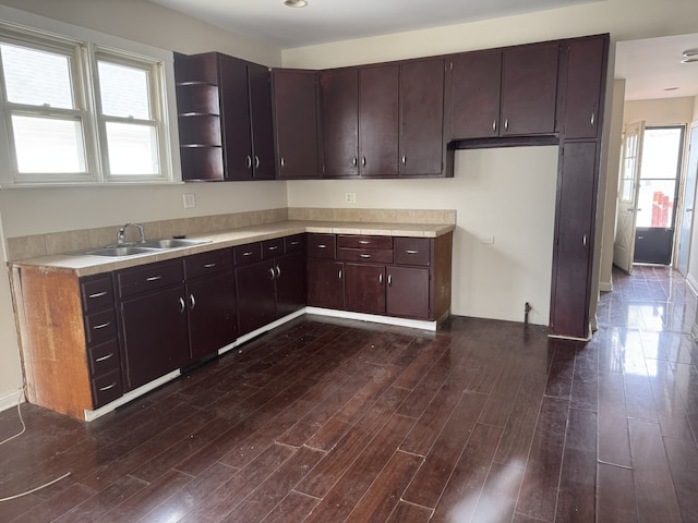 kitchen with open shelves, a sink, dark brown cabinets, light countertops, and dark wood-type flooring