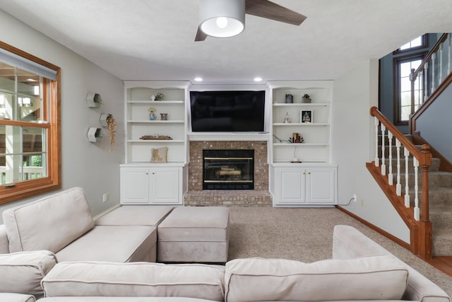 living room with a ceiling fan, built in features, a brick fireplace, stairway, and baseboards