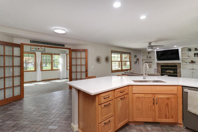 kitchen featuring a sink, dishwasher, a brick fireplace, a ceiling fan, and open floor plan