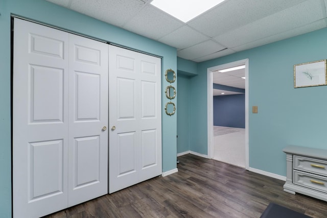 unfurnished bedroom featuring baseboards, a drop ceiling, a closet, and dark wood finished floors