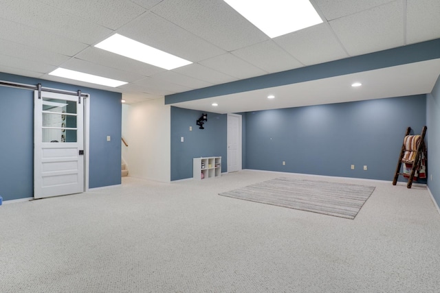 finished below grade area with carpet flooring, stairs, a barn door, and a paneled ceiling
