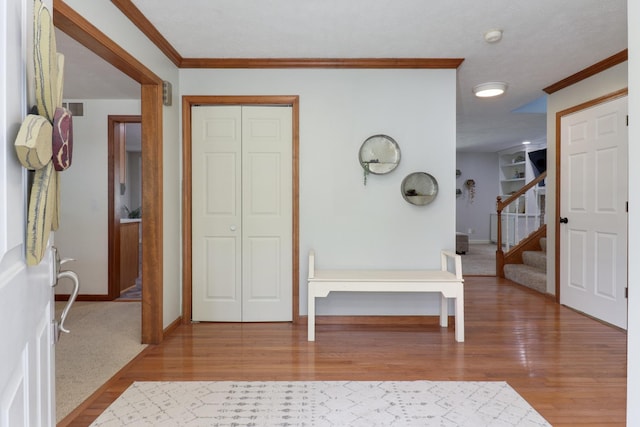 foyer entrance with crown molding, baseboards, wood finished floors, and visible vents
