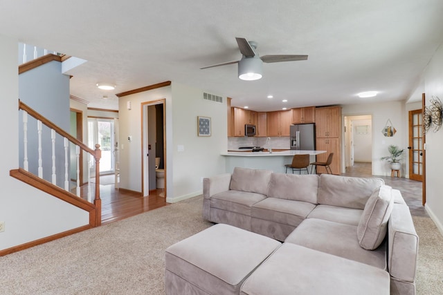 living area with ceiling fan, light carpet, stairs, baseboards, and visible vents