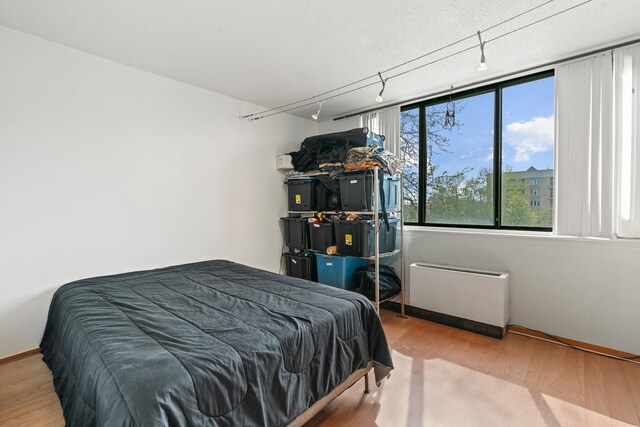 bedroom featuring rail lighting, radiator heating unit, and wood finished floors
