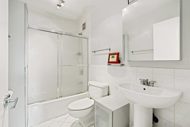 full bath featuring tile walls, tile patterned flooring, bath / shower combo with glass door, and toilet