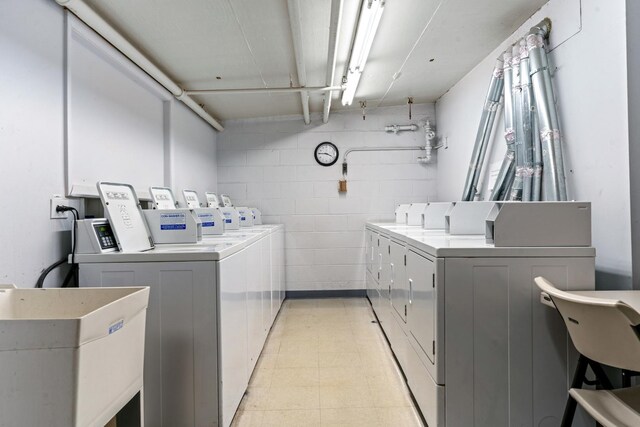community laundry room with concrete block wall, a sink, and washer and clothes dryer
