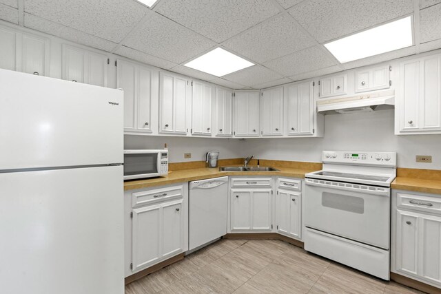 kitchen featuring a paneled ceiling, a sink, white cabinets, under cabinet range hood, and white appliances