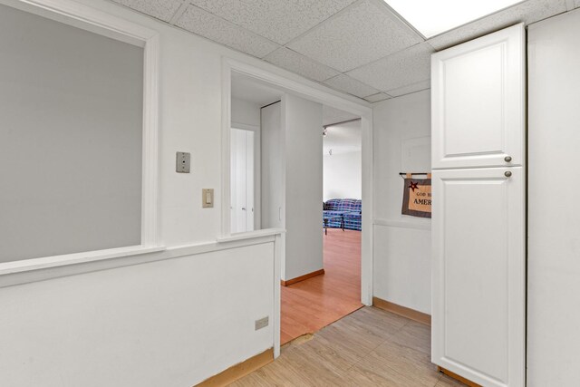 hallway with baseboards, light wood-style flooring, and a drop ceiling