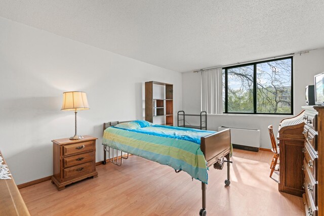 bedroom with a textured ceiling, baseboards, and light wood finished floors