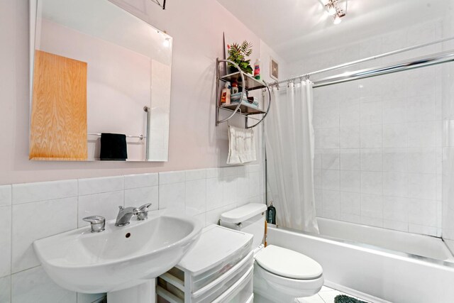 full bath featuring a sink, tile walls, shower / bath combo with shower curtain, and toilet