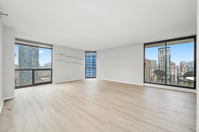 empty room featuring plenty of natural light, a view of city, floor to ceiling windows, and wood finished floors
