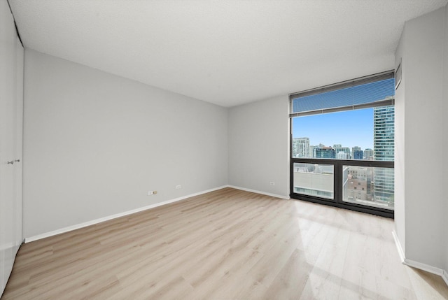 empty room featuring baseboards, a city view, floor to ceiling windows, and wood finished floors