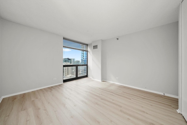 empty room with visible vents, a wall of windows, baseboards, light wood-type flooring, and a city view