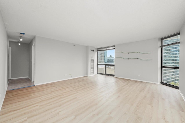 unfurnished living room with a wall of windows, baseboards, and light wood-style flooring