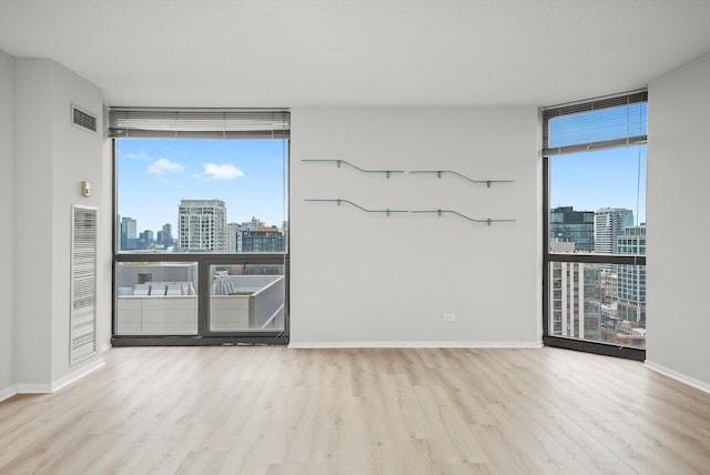 empty room with a wall of windows, baseboards, wood finished floors, visible vents, and a city view