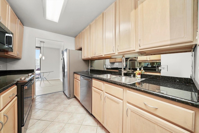 kitchen featuring appliances with stainless steel finishes, a sink, light brown cabinets, dark stone counters, and light tile patterned floors