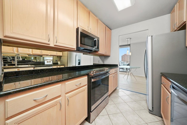 kitchen featuring a sink, light tile patterned floors, dark stone countertops, light brown cabinets, and stainless steel appliances