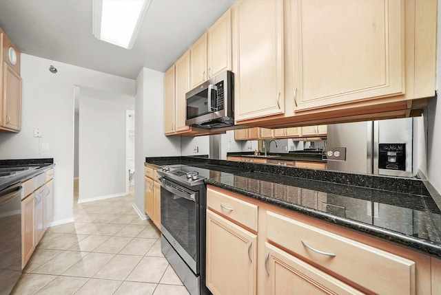 kitchen featuring baseboards, dark stone counters, appliances with stainless steel finishes, and light tile patterned flooring