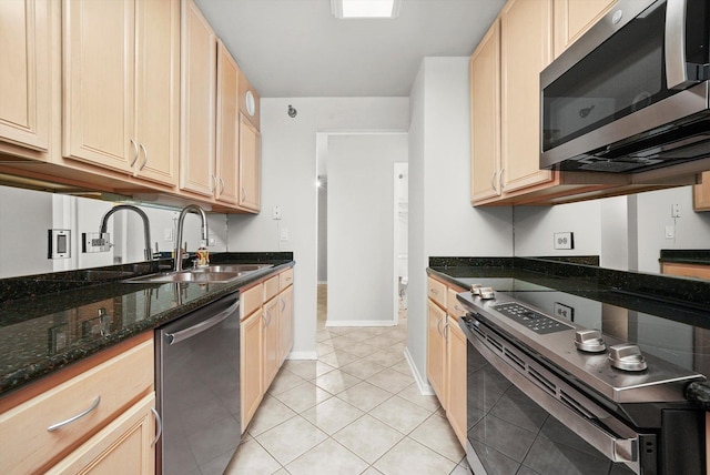 kitchen with light tile patterned flooring, a sink, dark stone countertops, stainless steel appliances, and baseboards