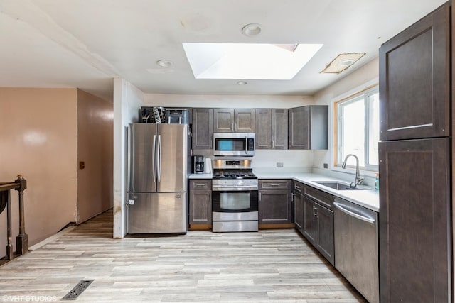kitchen featuring a skylight, dark brown cabinets, a sink, light countertops, and stainless steel appliances