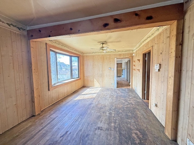 empty room featuring wood walls, wood finished floors, and a ceiling fan
