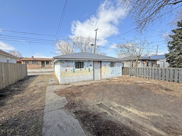 rear view of house with a shingled roof, concrete block siding, and fence