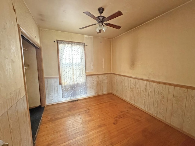 empty room with visible vents, wooden walls, wood finished floors, a ceiling fan, and wainscoting