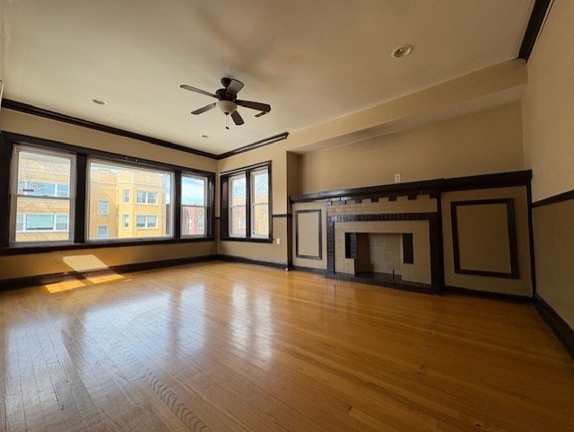unfurnished living room featuring wood finished floors, ornamental molding, a fireplace, baseboards, and a ceiling fan