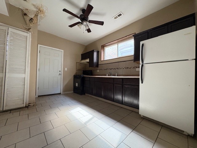 kitchen with freestanding refrigerator, light tile patterned floors, ceiling fan, dark cabinetry, and visible vents