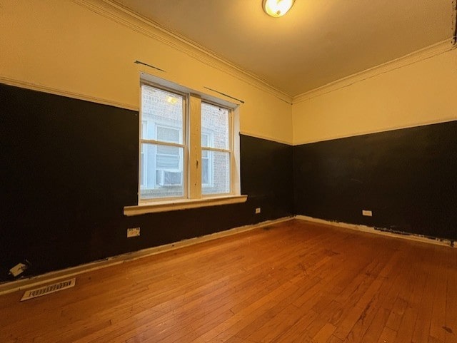 spare room with hardwood / wood-style flooring, visible vents, crown molding, and baseboards