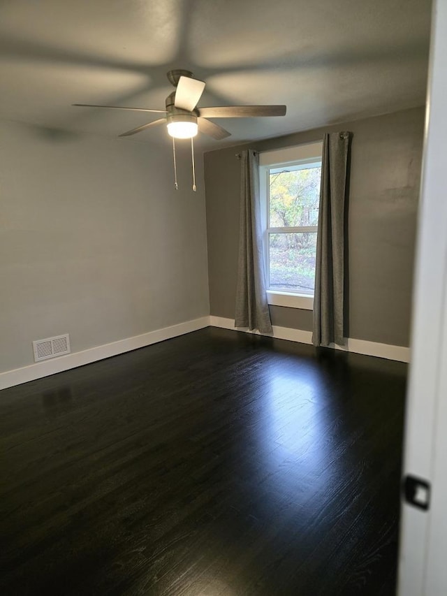 spare room featuring dark wood finished floors, a ceiling fan, visible vents, and baseboards