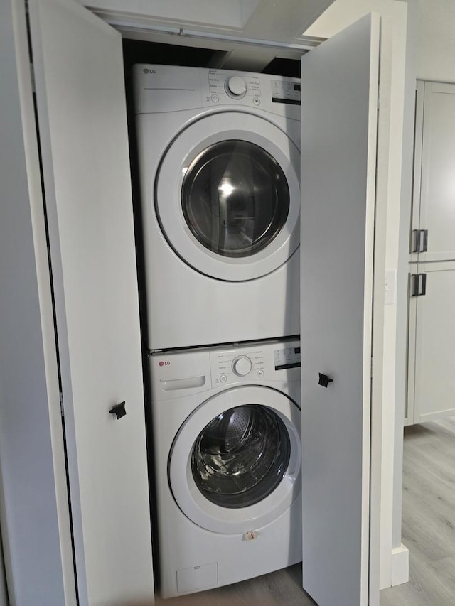 clothes washing area with stacked washing maching and dryer, wood finished floors, and laundry area