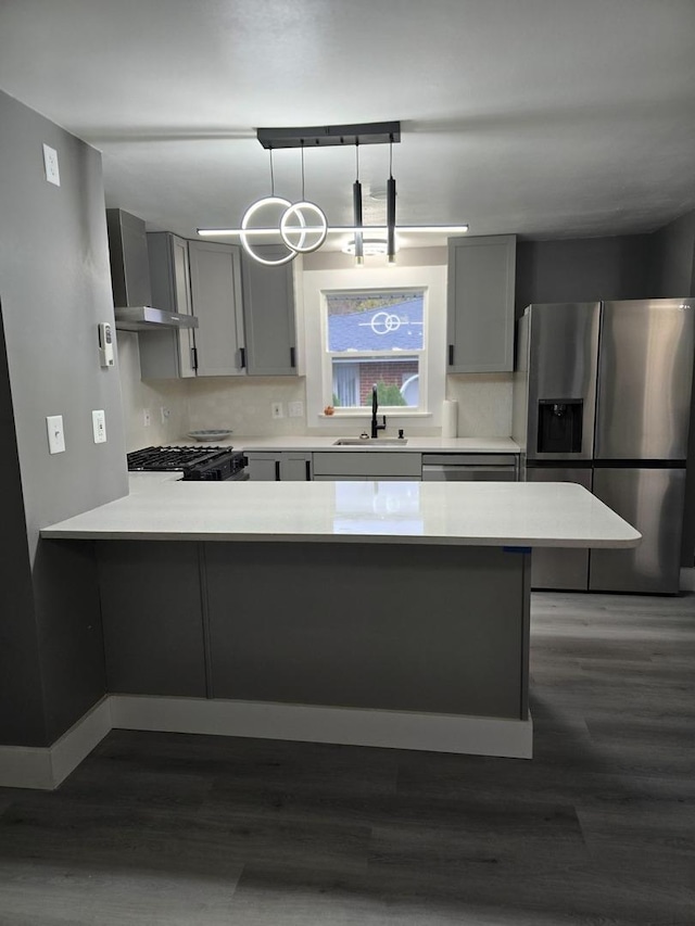 kitchen with a sink, stainless steel fridge, gray cabinets, and wall chimney range hood