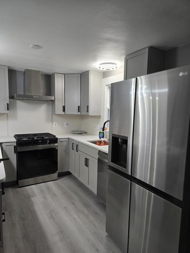 kitchen with a sink, appliances with stainless steel finishes, light countertops, light wood finished floors, and wall chimney exhaust hood
