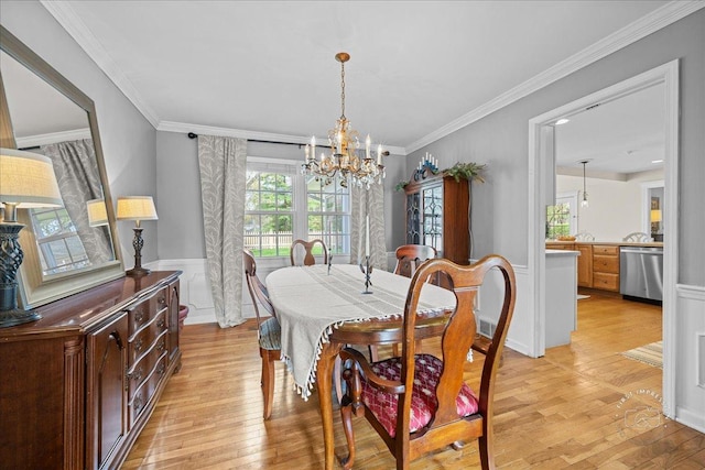 dining room with crown molding, a chandelier, light wood finished floors, and a wainscoted wall
