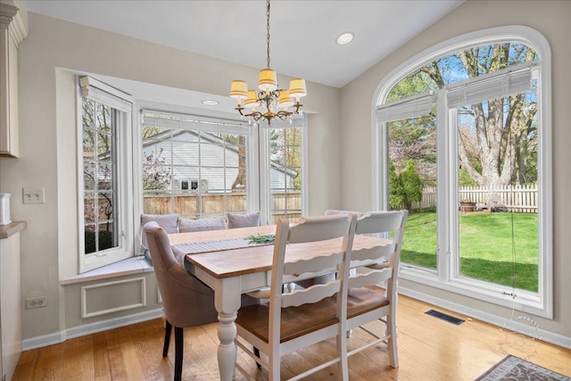 dining space with an inviting chandelier, light wood finished floors, baseboards, vaulted ceiling, and visible vents