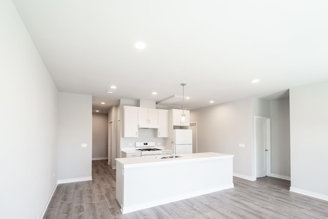 kitchen with light wood finished floors, a sink, white appliances, light countertops, and an island with sink
