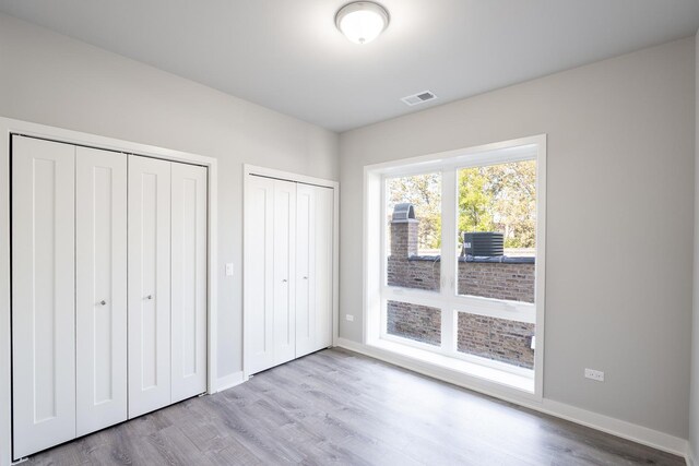 unfurnished bedroom with wood finished floors, two closets, visible vents, and baseboards