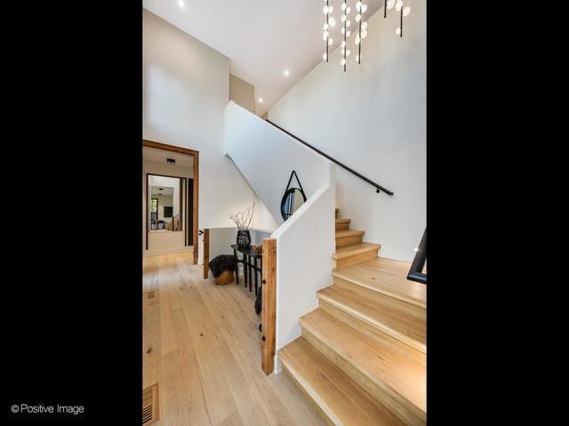 stairs with a towering ceiling, wood finished floors, recessed lighting, and a chandelier