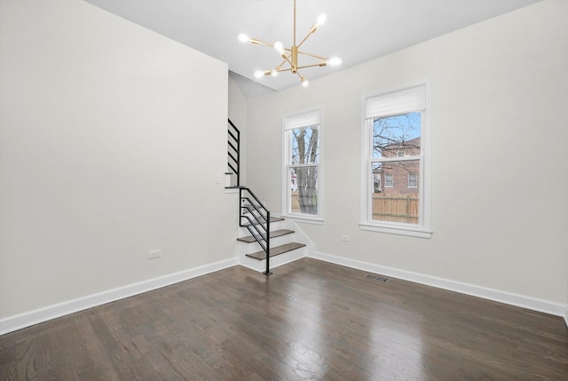 spare room with an inviting chandelier, visible vents, stairs, wood finished floors, and baseboards