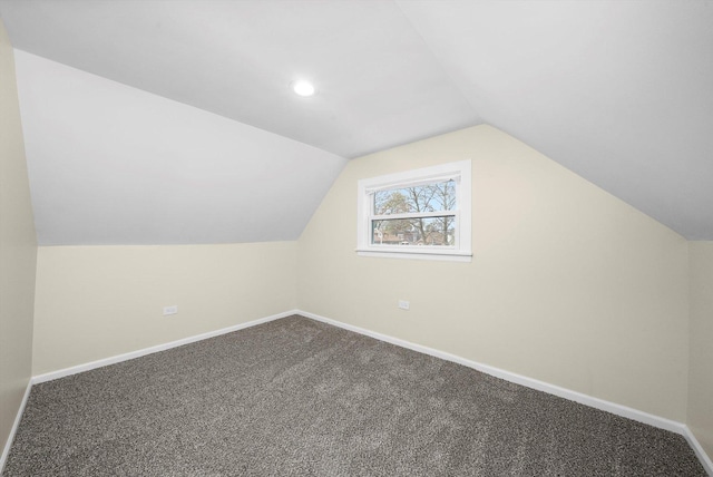 additional living space with baseboards, vaulted ceiling, and dark colored carpet