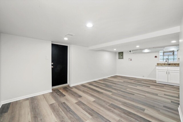 basement with electric panel, a sink, baseboards, light wood finished floors, and recessed lighting