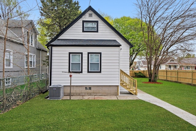 back of property with a fenced backyard, central AC, a yard, and a shingled roof